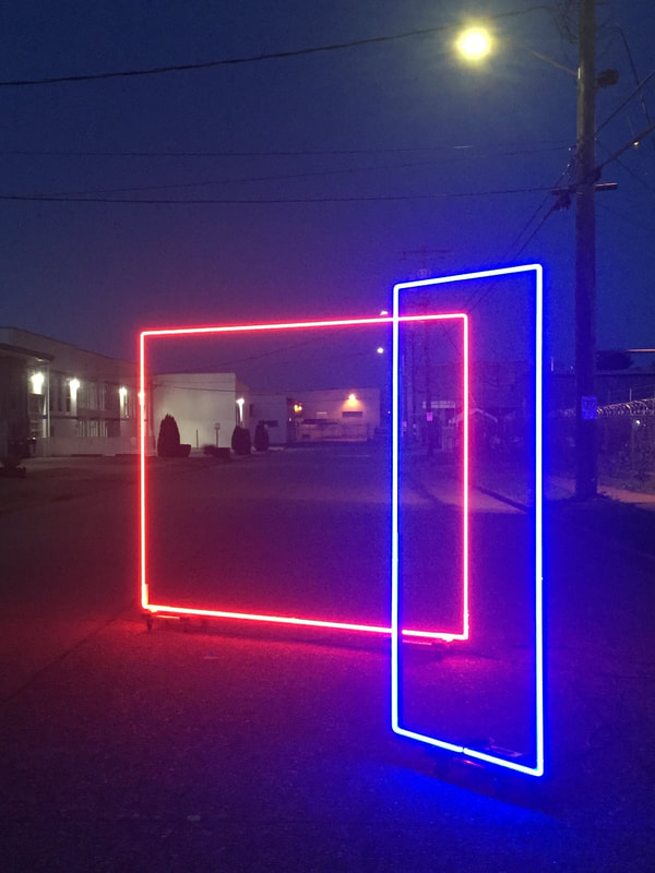 Artist photo of in process work: two colored neon rectangles: one blue and one red. Photo taken outside at night.